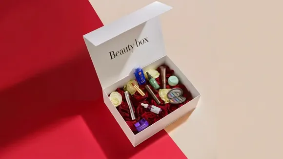 A white box labeled “Beauty box” contains assorted beauty products and artificial roses, placed on a red and beige split background.