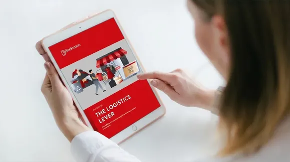 A person holds a tablet displaying a red screen with the title “The Logistics Lever” and an illustration of people moving boxes near a storefront.