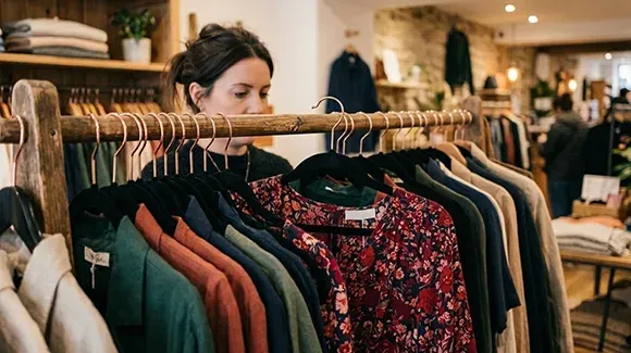 A woman browsing clothing on a wooden rack in a retail shop.