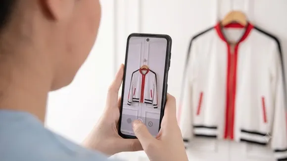 Person taking a photo of a white jacket with red and black trim, which is hanging on a wooden hanger, using a smartphone.