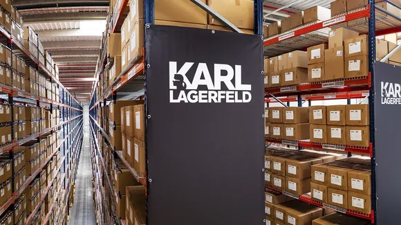 Warehouse shelves filled with brown boxes, with a black banner displaying the KARL LAGERFELD brand name attached to one shelving unit.