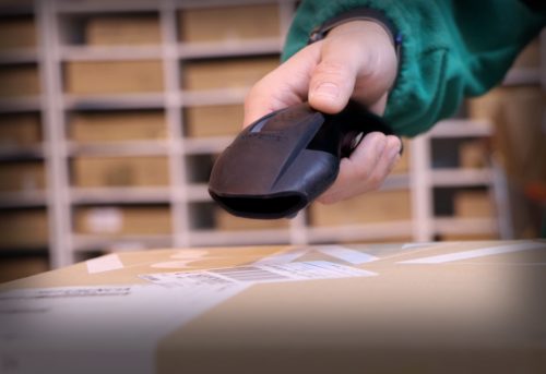 Person using a barcode scanner on a cardboard package in a storage area.