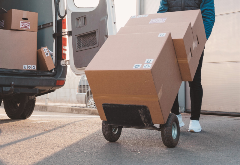 A worker transporting boxes on a cart through a warehouse.