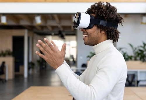 A person wearing a virtual reality headset and smiling, with hands raised, in a modern open office space.
