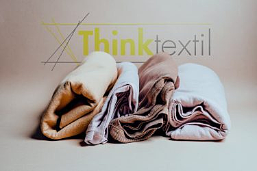 Three folded fabric rolls in beige and white shades are on display. The background has the text "Think Textil.