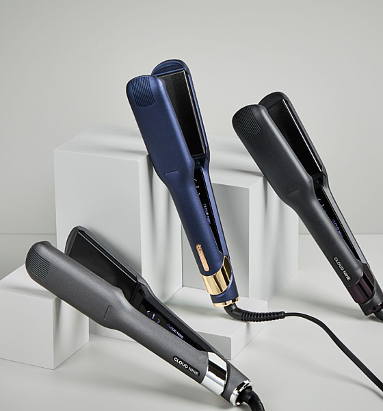 Three hair straighteners in black and blue are placed on white geometric blocks against a light gray background.