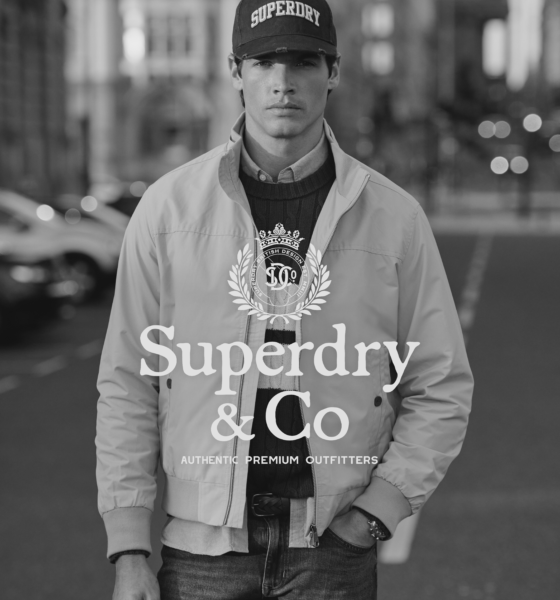 A man wearing a Superdry jacket, t-shirt, and cap stands on a city street. The Superdry & Co logo and text overlay the center of the image.