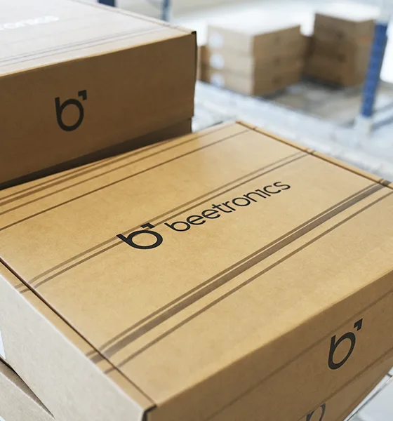 A close-up of a cardboard box labeled "beetronics" with other similar boxes stacked in the background.