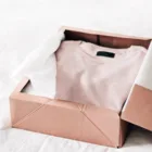 Pink t-shirt neatly folded in a cardboard box.