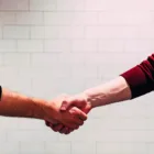 Two professionals engage in a firm handshake against a pristine white backdrop.