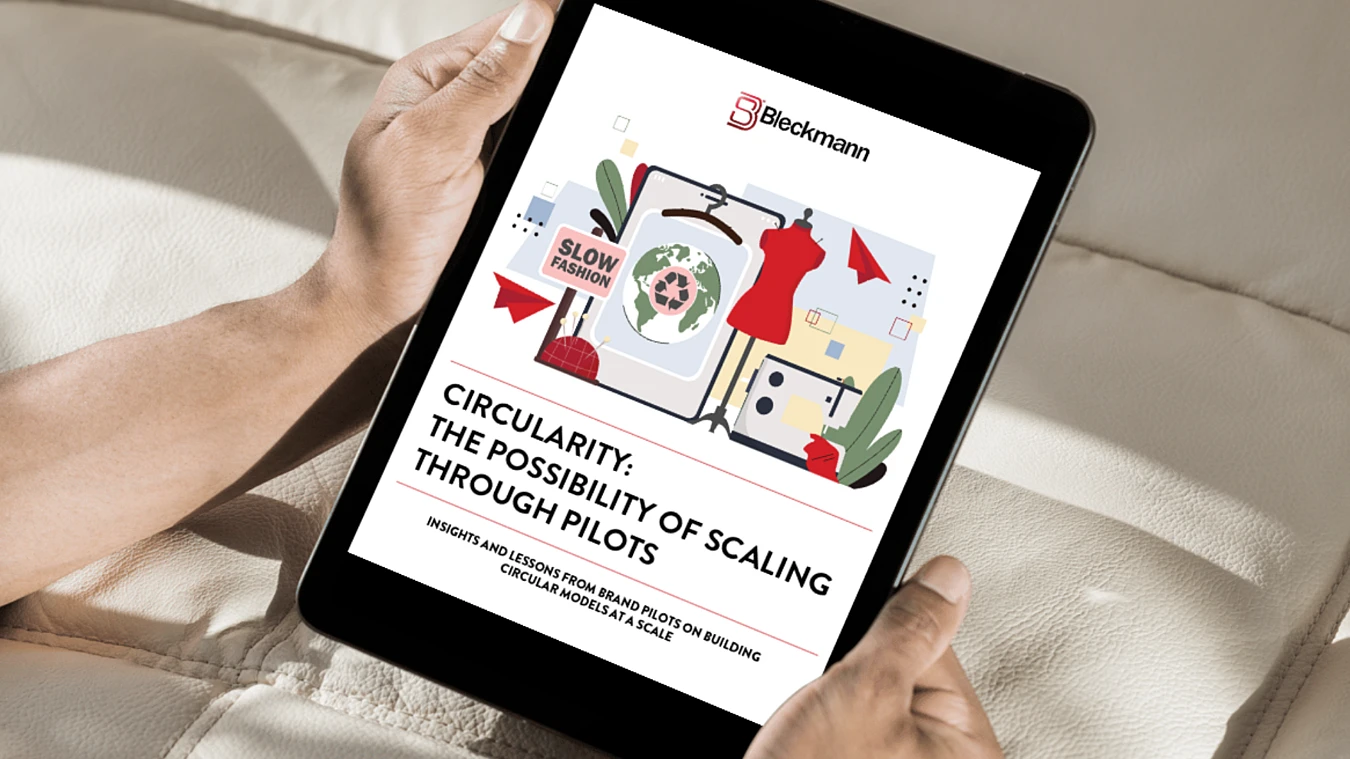 A person holds a tablet displaying a Bleckmann report titled “Circularity: The Possibility of Scaling Through Pilots,” featuring a clothing graphic and circular economy symbols.