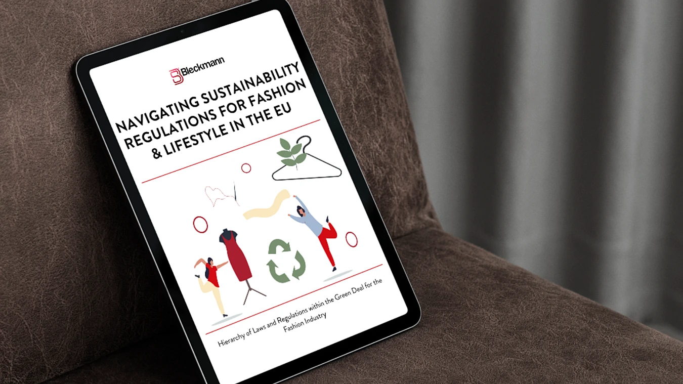 A tablet on a brown chair displays a document titled "Navigating Sustainability Regulations for Fashion & Lifestyle in the EU" with illustrated figures and sustainability icons on the cover.