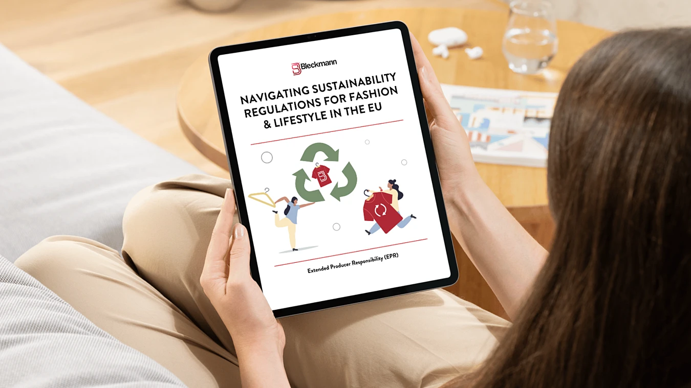 A person holds a tablet displaying a document titled "Navigating Sustainability Regulations for Fashion & Lifestyle in the EU" with illustrated icons of people and recycling symbols.