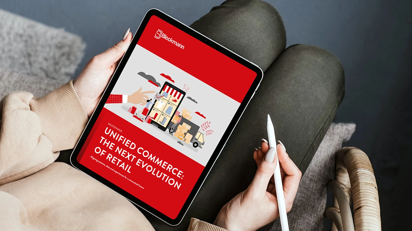 Person holding a tablet displaying a digital document titled "Unified Commerce: The Next Evolution of Retail" with retail-related illustrations on the cover.