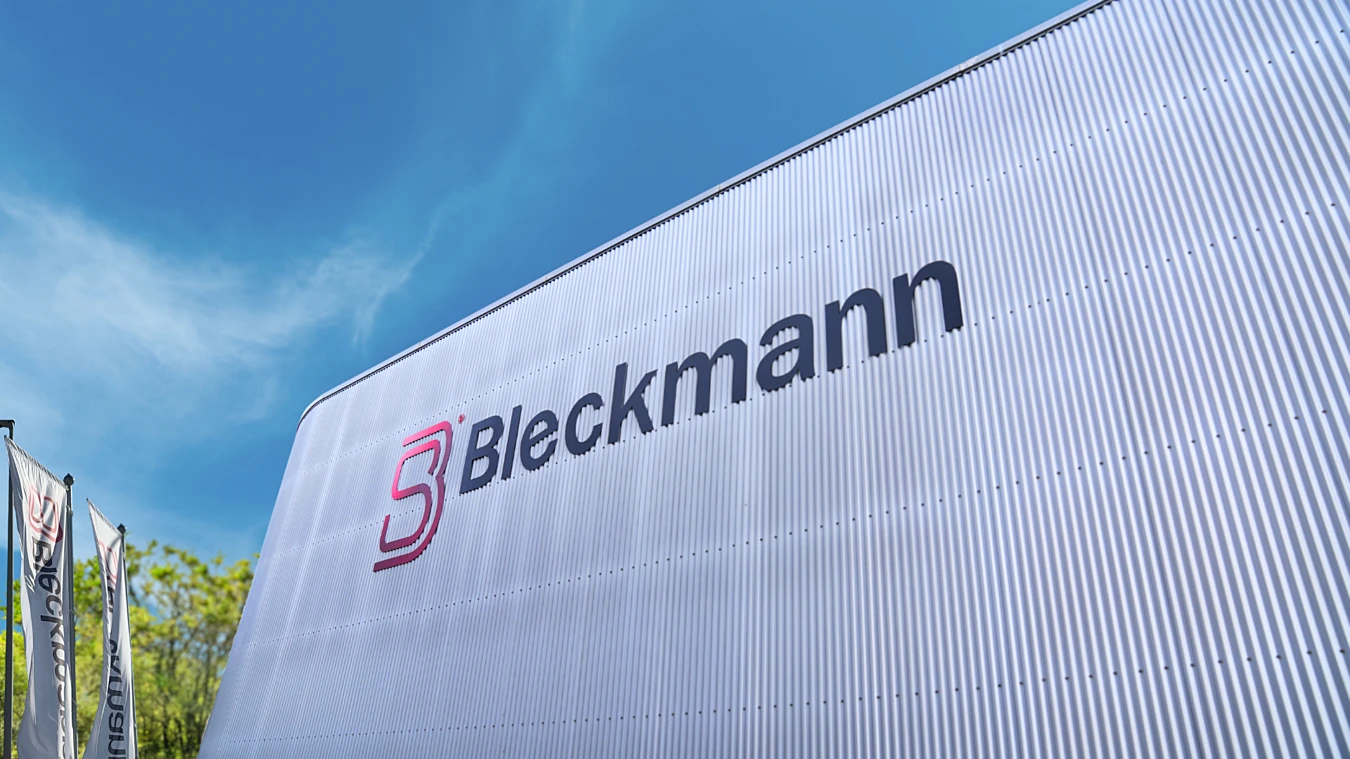 Large corrugated metal building with the Bleckmann logo and name on its side, set against a blue sky.