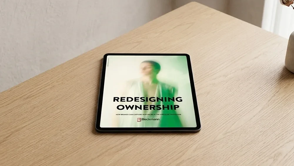 A tablet on a wooden desk displays a digital document titled "Redesigning Ownership" with a blurred image of a person in the background.