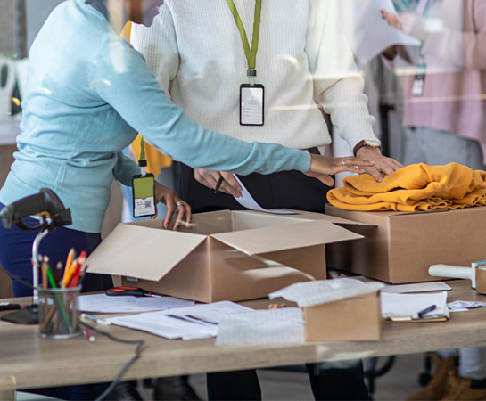 People at a table packing boxes, with papers, pens, and a phone visible.