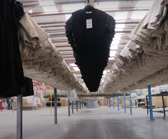 Rows of hanging black and beige garments in a spacious warehouse interior.