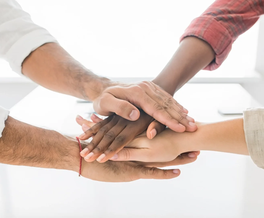 Four people stack their hands together in a gesture of teamwork against a bright background.
