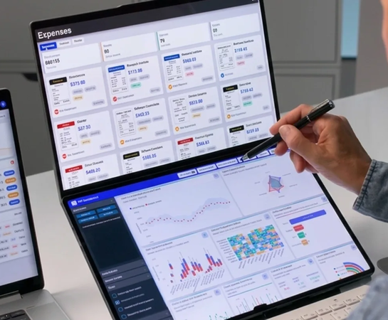Person using a dual-screen laptop displaying financial dashboards and analytics, with graphs, charts, and expense data visible on both screens.