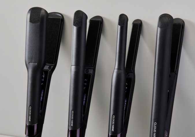 Four black hair straighteners of varying sizes are standing upright against a light background.