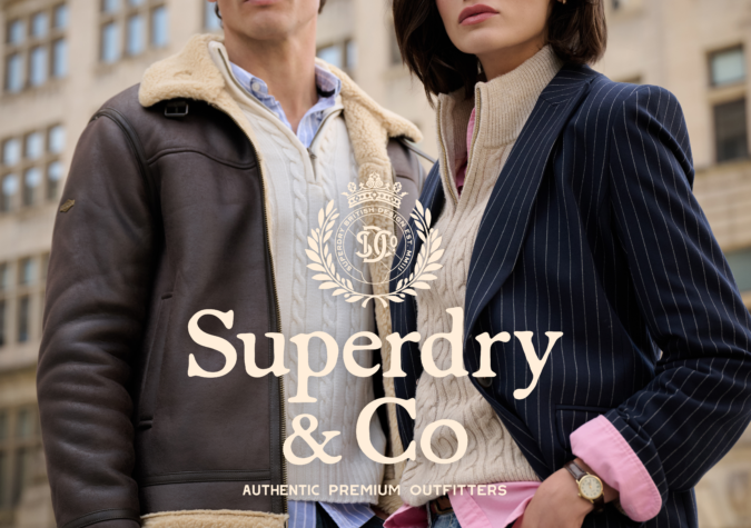 A man and a woman stand outdoors in casual, layered clothing. Both wear jackets over sweaters and collared shirts. City buildings appear in the background. "Superdry & Co" logo overlays the image.