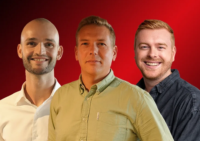 Three men stand side by side, facing forward, in front of a red background. The man in the middle wears a green shirt, while the other two are in white and dark shirts.