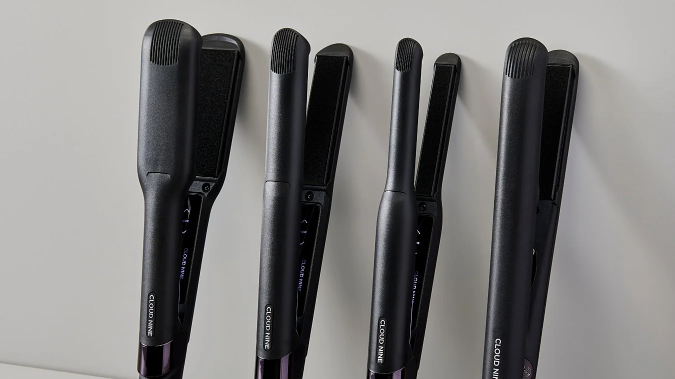 Four black hair straighteners of varying sizes are standing upright against a light background.
