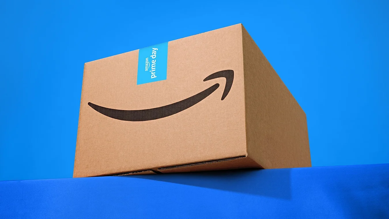 A cardboard Amazon box with a Prime Day label sits on a blue surface against a blue background.
