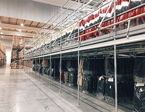 Spacious warehouse interior with stacked shelves holding wrapped clothing items, lit by overhead lights.