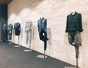 Mannequins displaying various casual outfits, including denim jackets, gray tracksuits, and a floral skirt with a green jacket, against a beige wall.