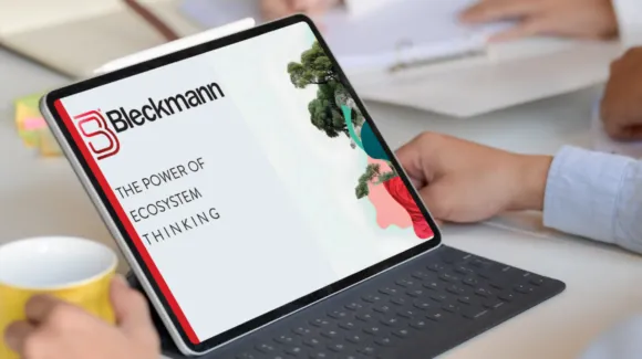 Tablet displaying a presentation titled "The Power of Ecosystem Thinking" with the Bleckmann logo. Hands holding the tablet, background shows people and desk with papers.