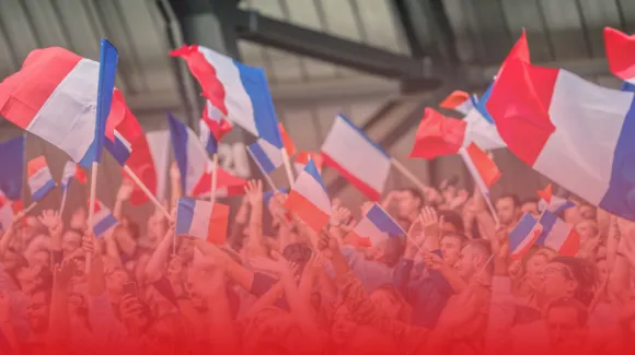 A crowd of people waving red, white, and blue flags indoors, with a heavy red tint at the bottom of the image.