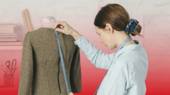 A woman measures the back length of a brown jacket on a dress form using a tape measure.