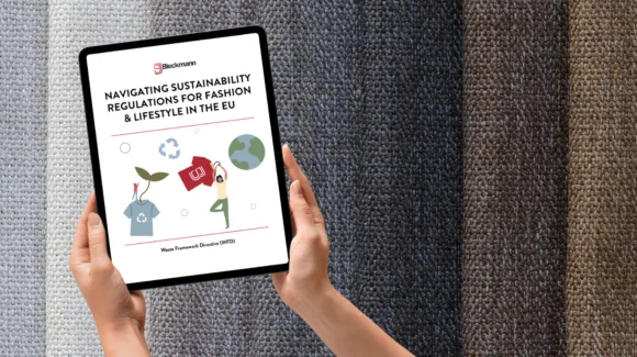 A person holds a tablet displaying a document titled "Navigating Sustainability Regulations for Fashion & Lifestyle in the EU" against a background of textured fabric in various colors.