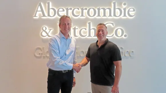 Two men shake hands in front of an illuminated Abercrombie & Fitch Co. sign inside a corporate office.