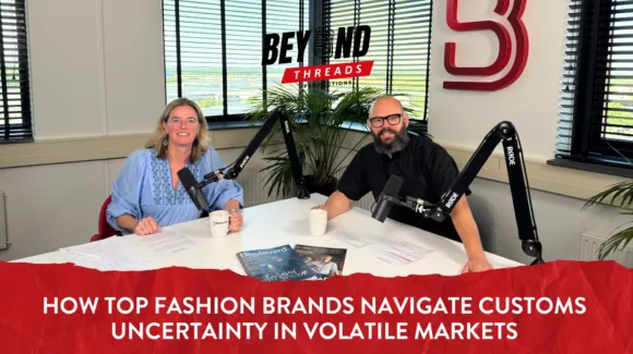 Two podcast hosts sit at a table with microphones, notes, and coffee mugs. Text overlay discusses how fashion brands handle customs uncertainty in volatile markets.