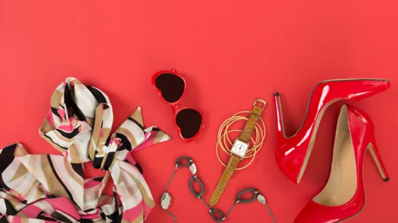 Scarf, heart-shaped sunglasses, necklace, watch, bracelet, and red high-heeled shoes arranged on a red background.