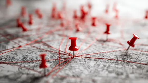 A close-up of a map with red push pins connected by red string, illustrating a network or connections between multiple locations.