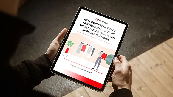Person holding a tablet displaying a Dutch-language article titled “Het Doorbreken van de Fast Fashion-Cyclus: De Wereldwijde Opkomst van de Resale Economie” with an illustration of clothes.