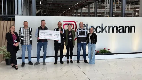 Seven people stand in a row indoors; one holds a large check. They pose in front of a sign that reads "Blockmann.