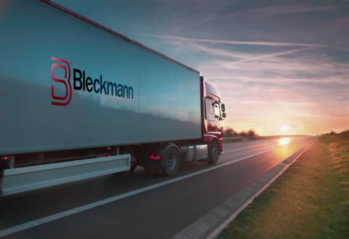 A Bleckmann-branded semi-truck drives on an empty highway at sunset, with the sky displaying clouds and contrails.