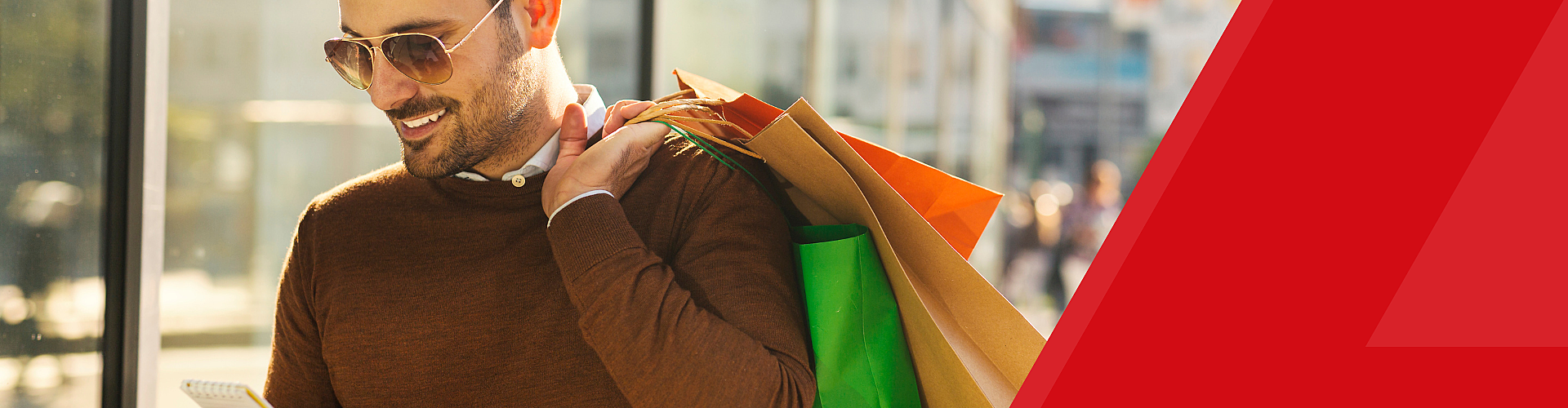 Man in sunglasses holding shopping bags and checking his phone.