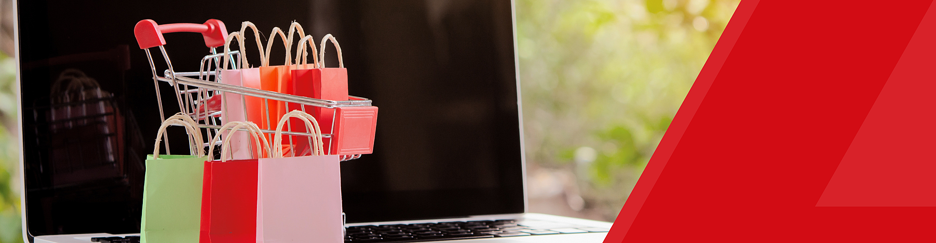 A miniature shopping cart with colorful bags sits on a laptop keyboard, featuring a red diagonal design on the right.