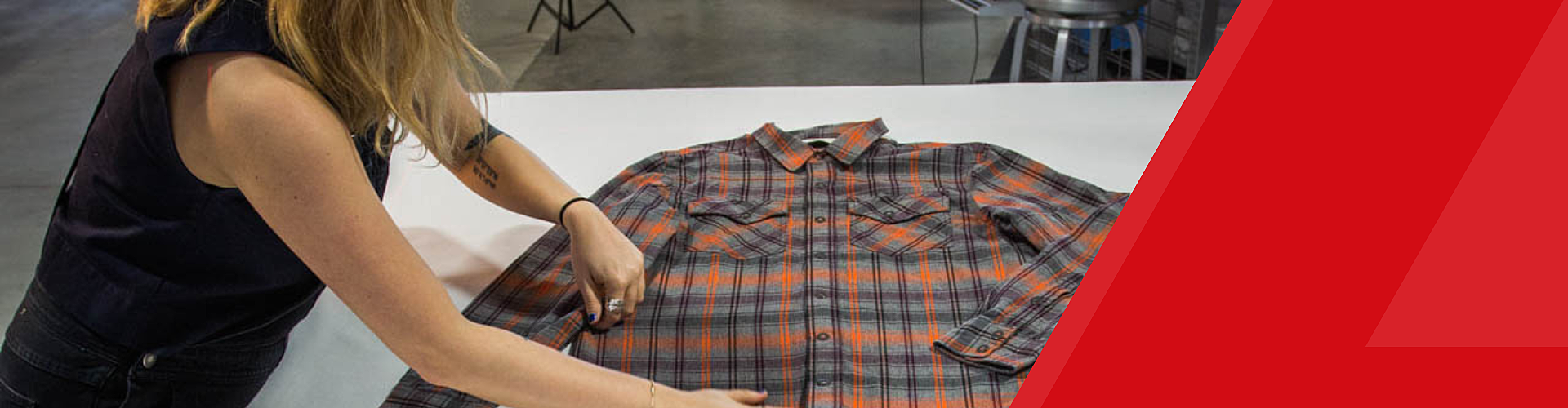 A person arranges a plaid flannel shirt on a white surface.