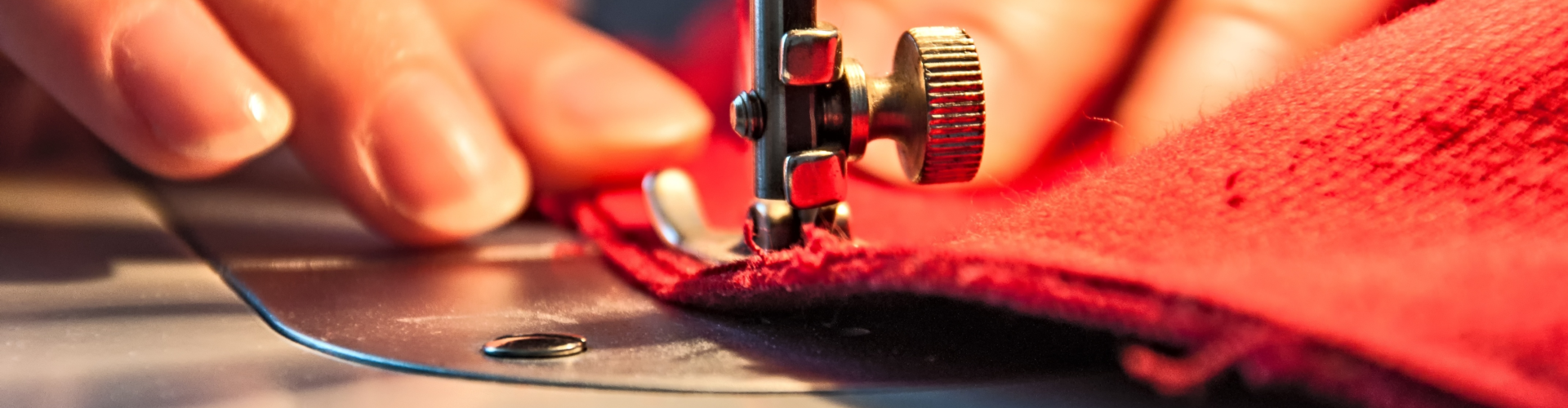 Close-up of hands guiding red fabric through a sewing machine, with a focus on the needle and presser foot.