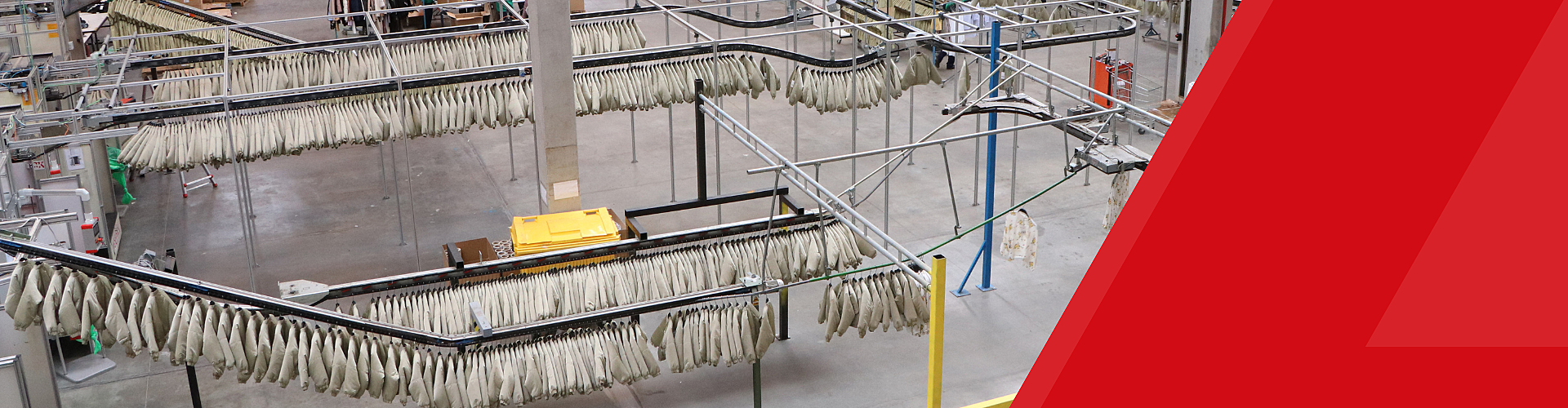 Industrial facility with rows of fish hanging from racks for drying, viewed from above, with concrete floors and red geometric overlay on the right side.