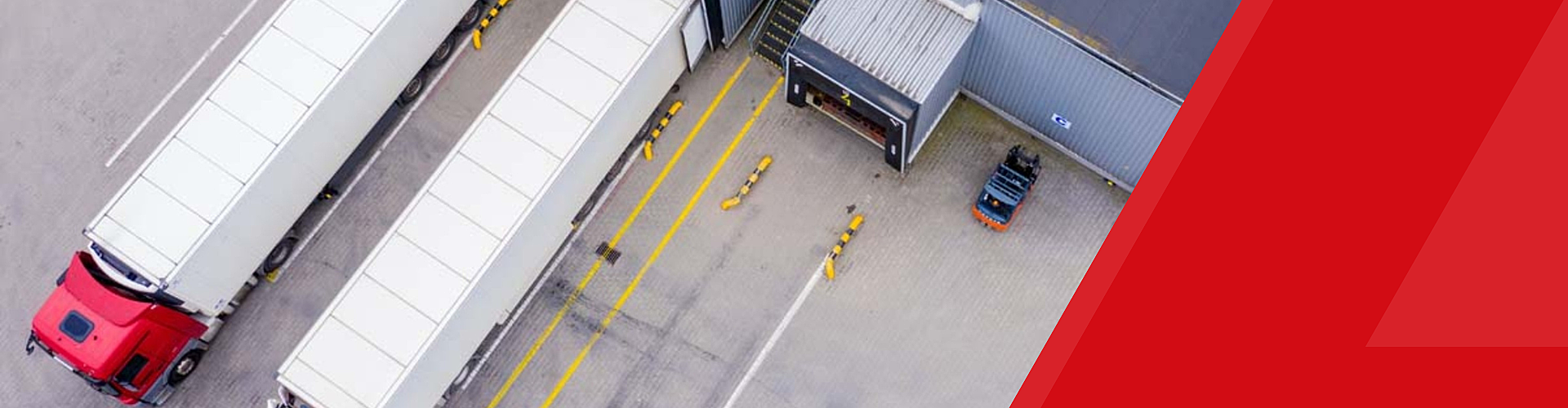 Aerial view of two large trucks parked at a loading dock next to a warehouse building, with a forklift nearby.