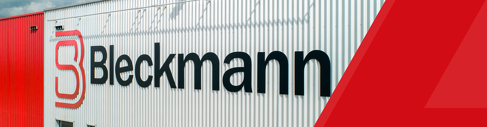 The exterior wall of a building features the Bleckmann logo and name in large black letters on white corrugated metal, with red siding and geometric design accents.