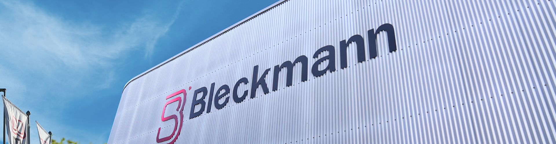 A large building with the Bleckmann logo and name on its corrugated exterior wall, photographed against a clear blue sky.